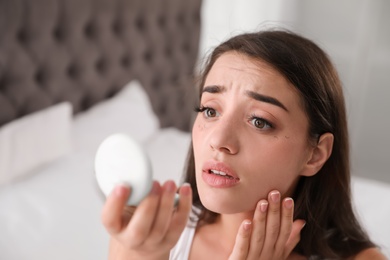 Photo of Young woman with eyelash loss problem looking in mirror indoors