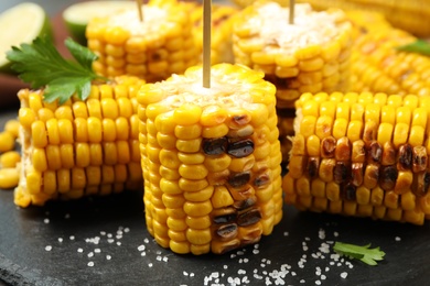 Photo of Tasty grilled corn on black plate, closeup