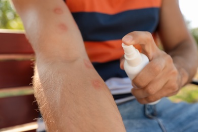 Photo of Man spraying insect repellent on his arm outdoors, closeup