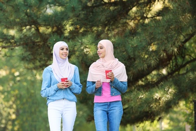 Photo of Muslim women with cups of coffee walking in park