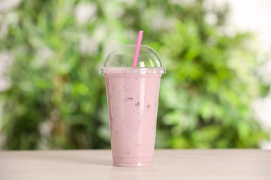 Photo of Plastic cup of tasty smoothie on wooden table outdoors