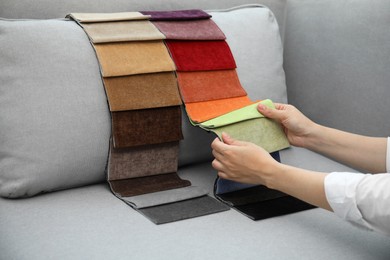 Woman choosing fabric among colorful samples on grey sofa, closeup