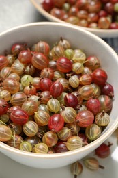 Photo of Fresh ripe gooseberries in bowls on light table, closeup
