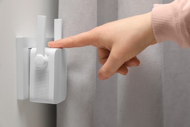 Woman turning on wireless Wi-Fi repeater indoors, closeup