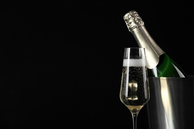 Photo of Glass of champagne near bucket with bottle on black background, space for text