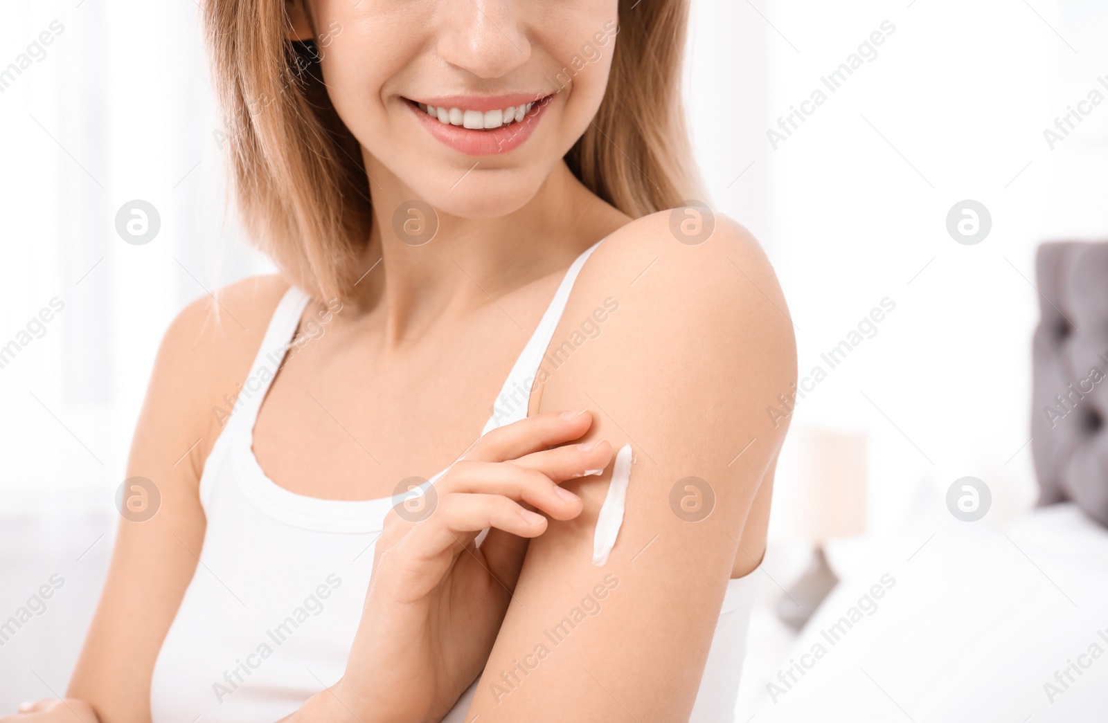 Photo of Young woman applying cream indoors, closeup. Beauty and body care