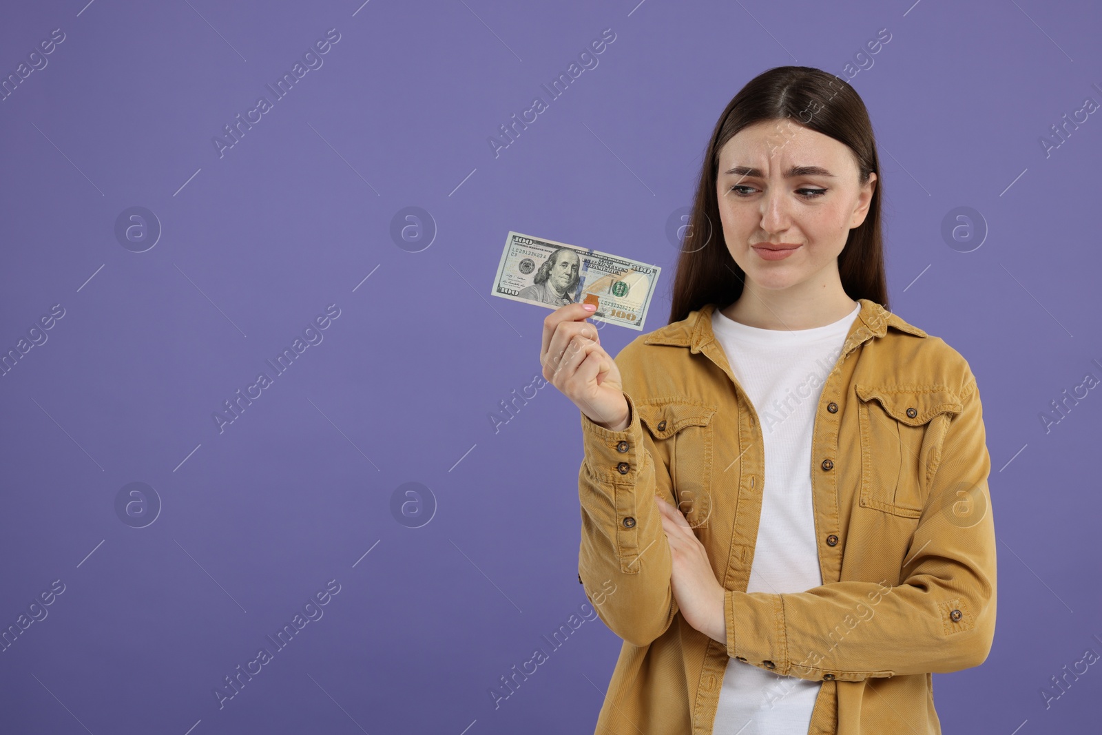 Photo of Sad woman with dollar banknote on purple background, space for text