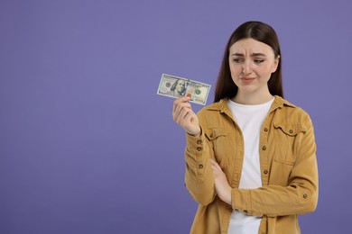 Sad woman with dollar banknote on purple background, space for text