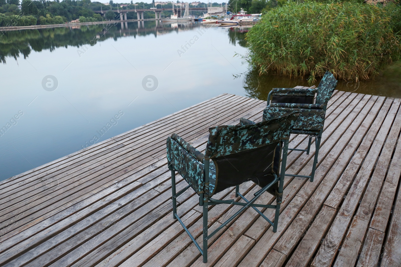 Photo of Camouflage fishing chairs on wooden pier near river, space for text