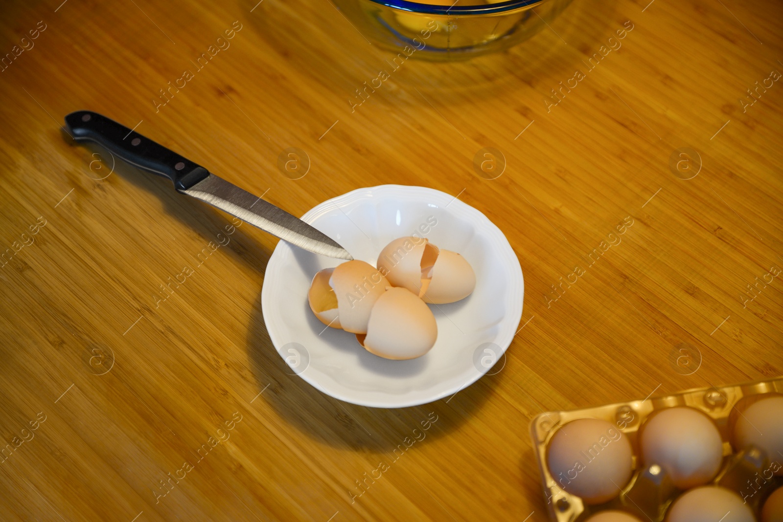 Photo of White plate with egg shells and knife on wooden table