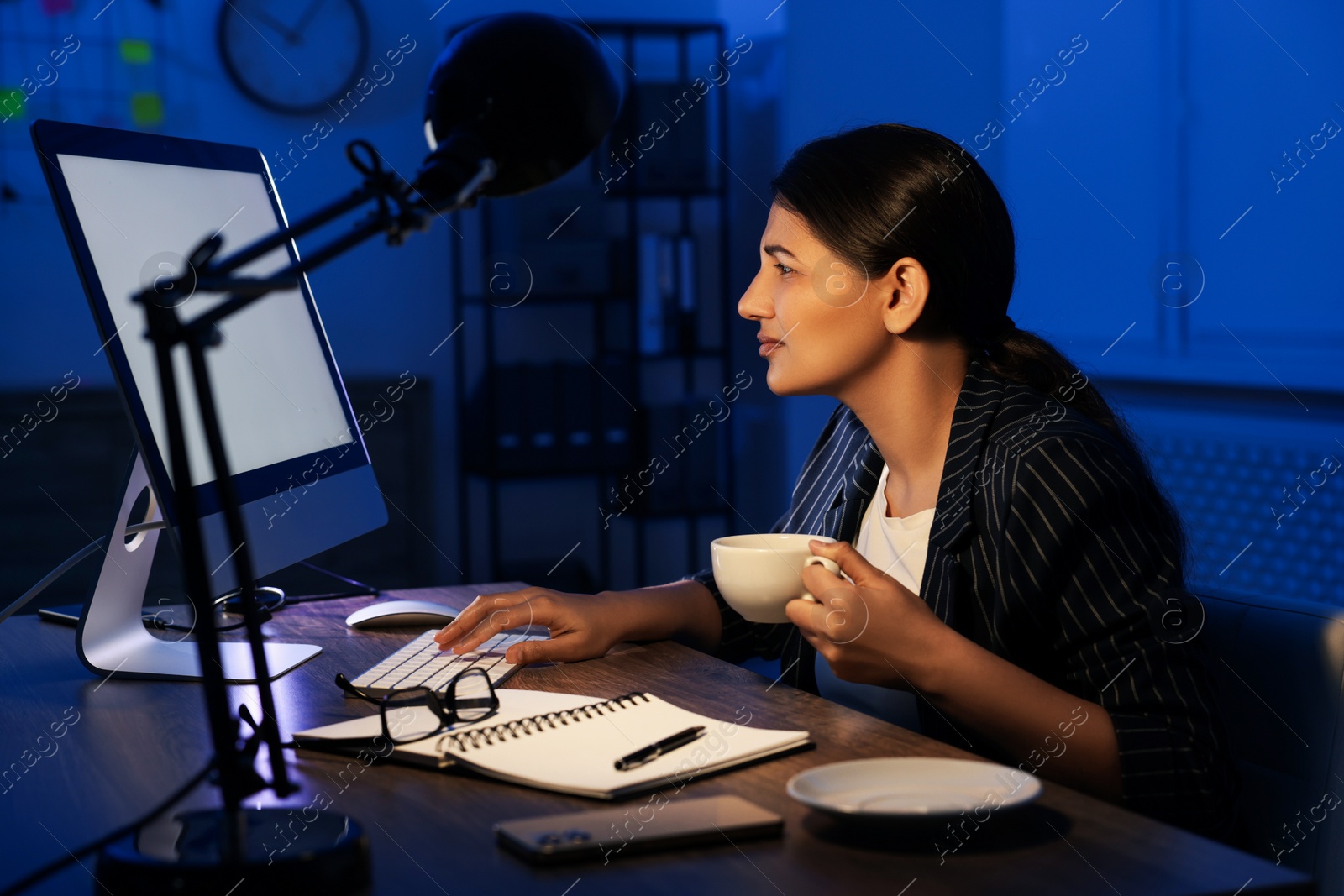 Photo of Tired overworked businesswoman drinking coffee at night in office