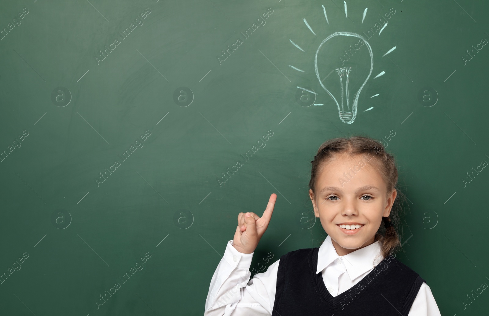 Photo of Little school child in uniform near chalkboard with lightbulb drawing