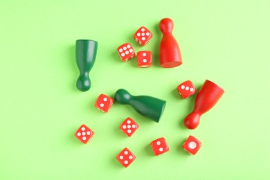 Many red dices and color game pieces on green background, flat lay