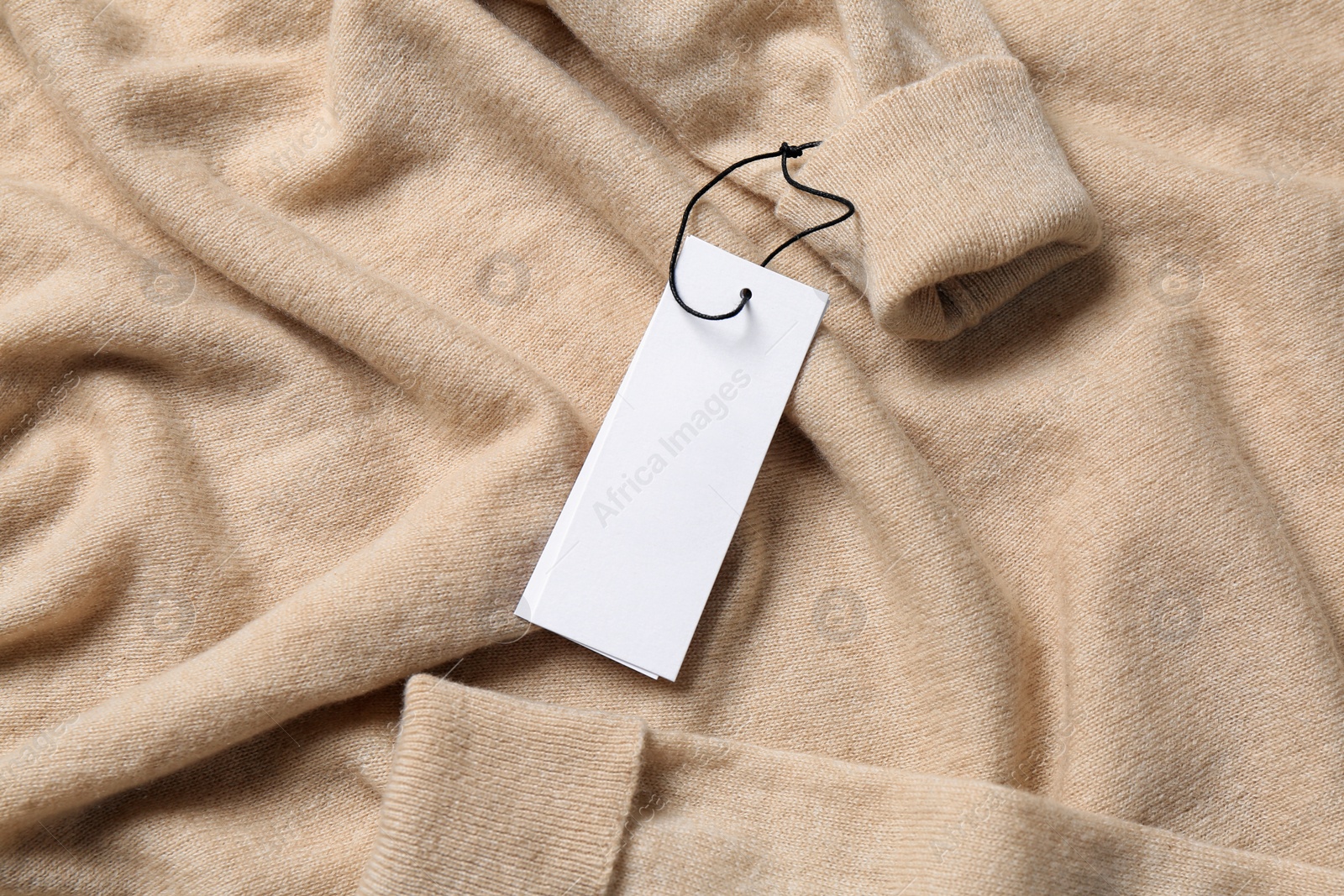 Photo of Blank white tags on beige sweater, top view. Space for text