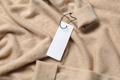 Blank white tags on beige sweater, top view. Space for text