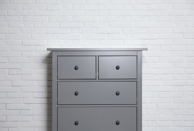 Grey chest of drawers near white brick wall indoors