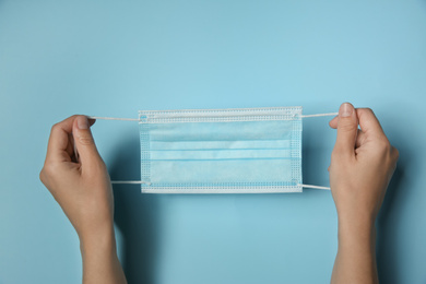 Photo of Woman holding disposable face mask on light blue background, closeup. Protective measures during coronavirus quarantine