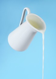 Pouring milk from jug on light blue background