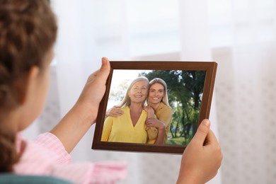 Image of Little girl holding frame with photo portrait of her family indoors, closeup