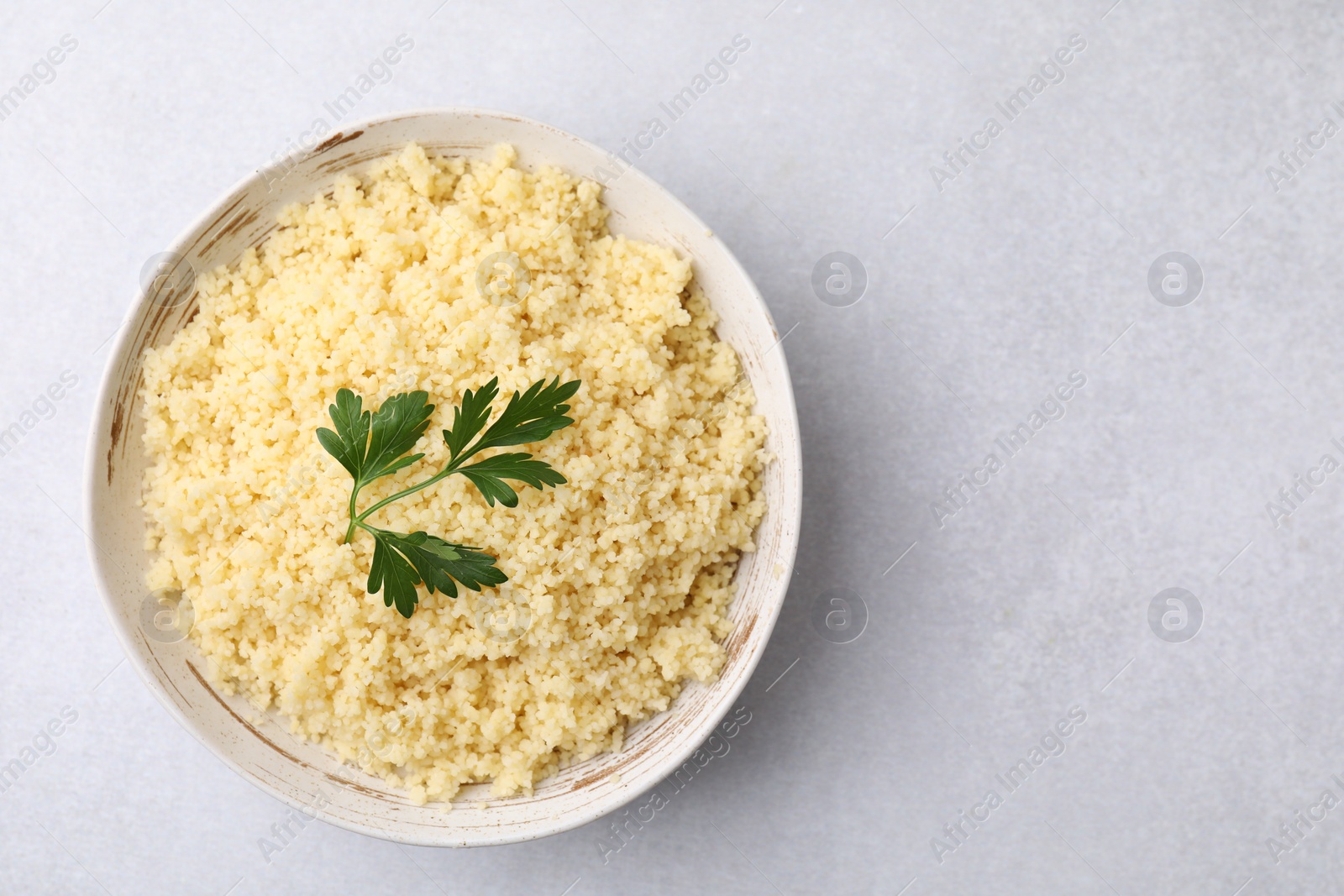 Photo of Tasty couscous and fresh parsley in bowl on light grey table, top view. Space for text