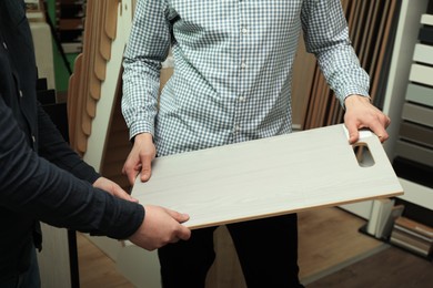 Photo of Men holding sample of wooden flooring in shop, closeup