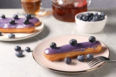 Tasty glazed eclairs with blueberries on grey marble table, closeup