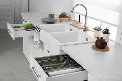 Photo of Open drawers with different utensils, towels and napkins in kitchen