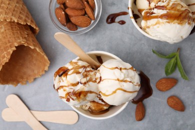 Scoops of ice cream with caramel sauce and nuts on light grey table, flat lay