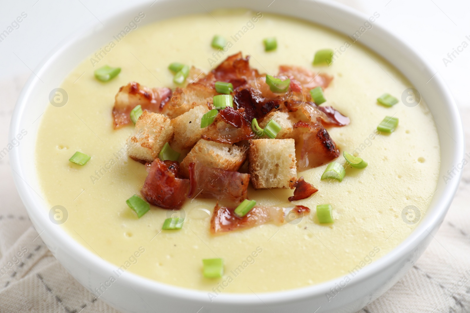 Photo of Tasty potato soup with bacon, green onion and croutons in bowl on white table, closeup