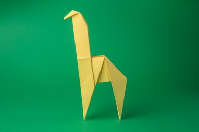 Photo of Origami art. Handmade yellow paper giraffe on green background