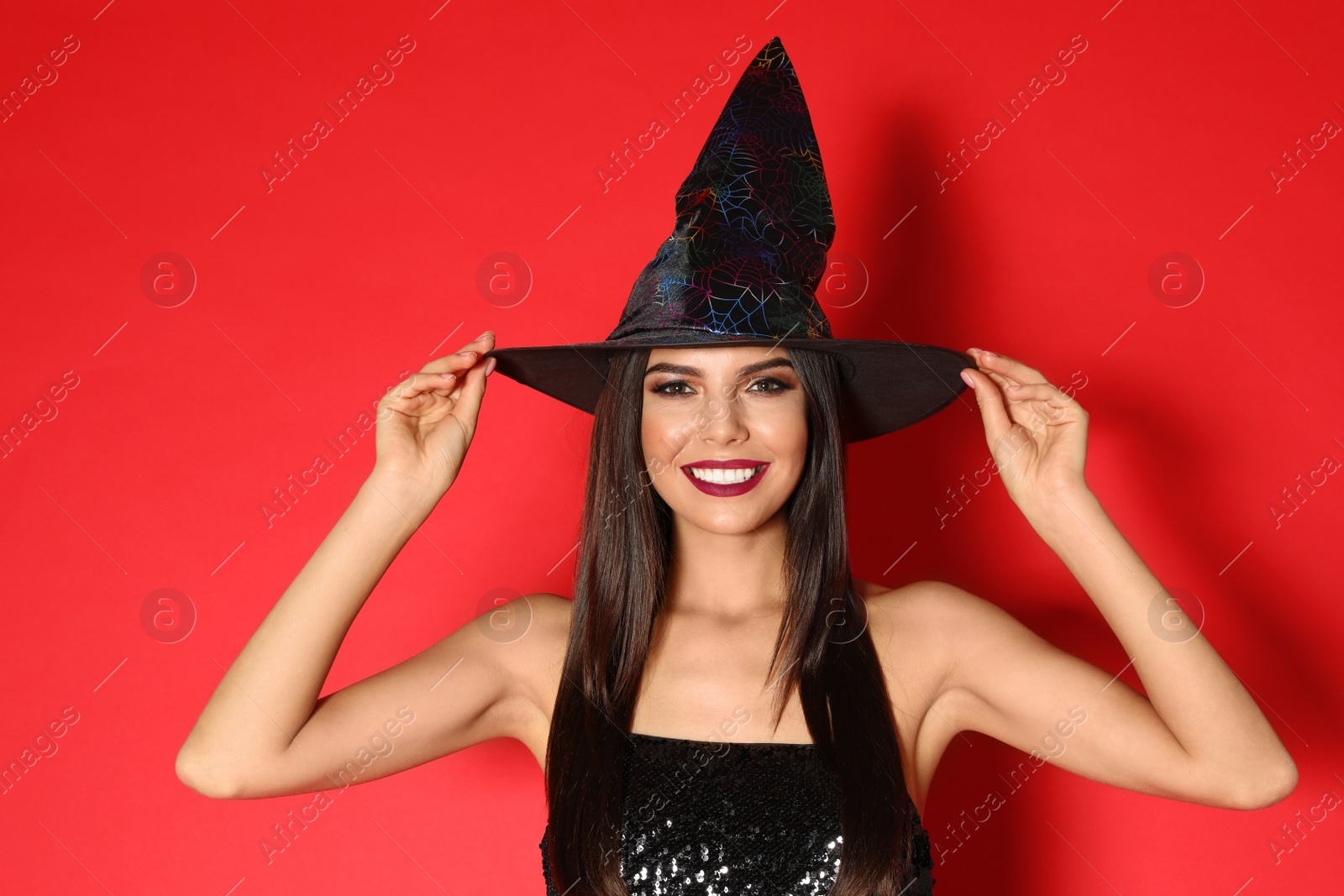 Photo of Beautiful young woman wearing witch costume for Halloween party on red background