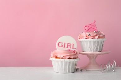 Baby shower cupcakes with toppers on white table against pink background, space for text