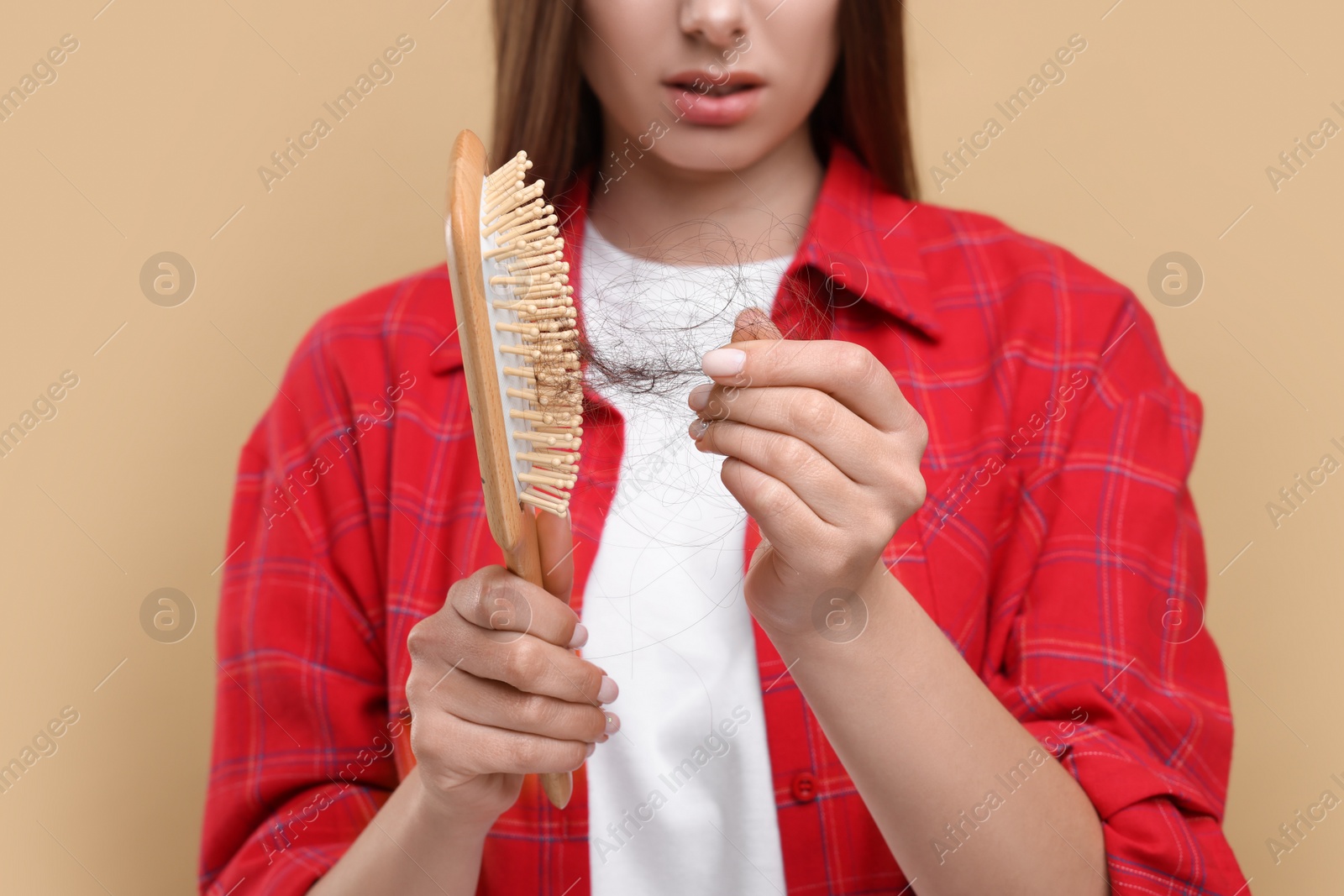 Photo of Woman untangling her lost hair from brush on beige background, closeup. Alopecia problem