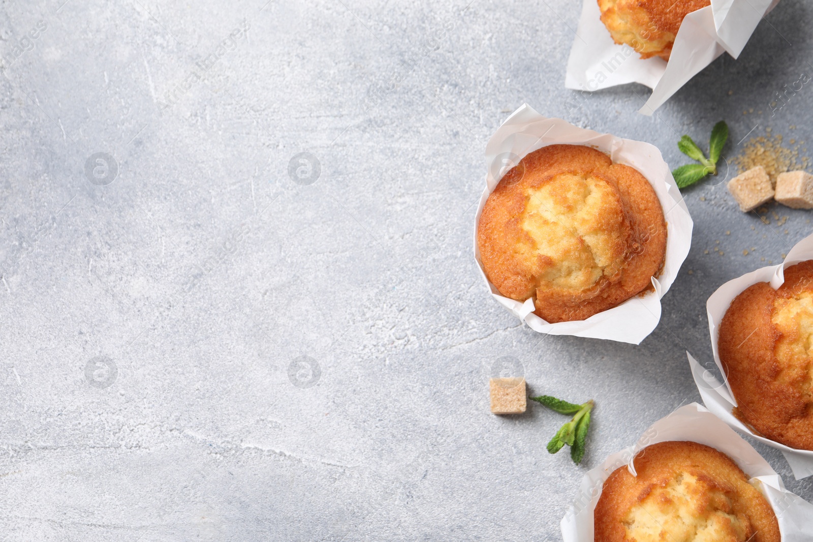 Photo of Delicious sweet muffins and brown sugar on light grey textured table, flat lay. Space for text