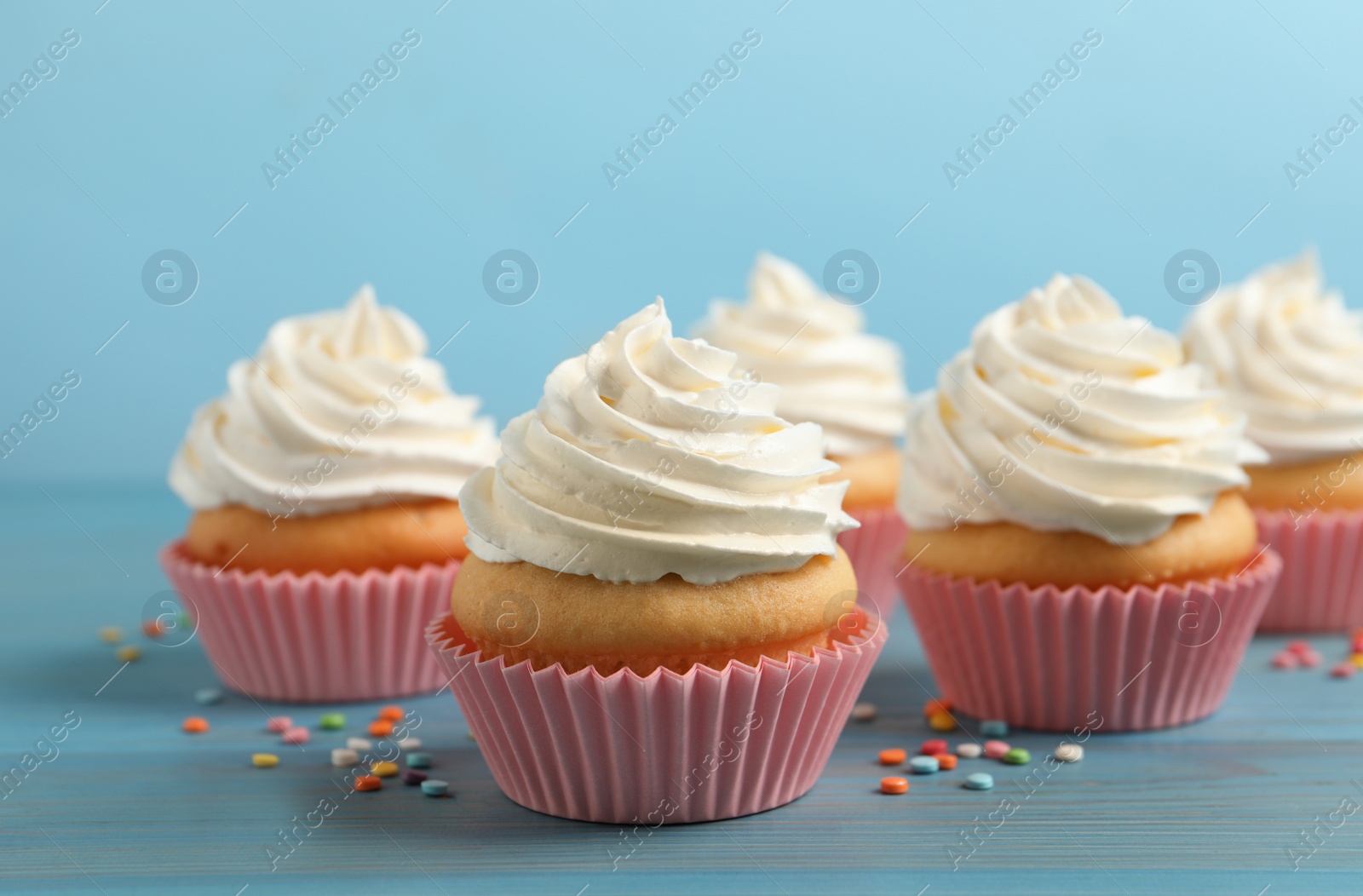 Photo of Delicious cupcakes decorated with cream on light blue wooden table