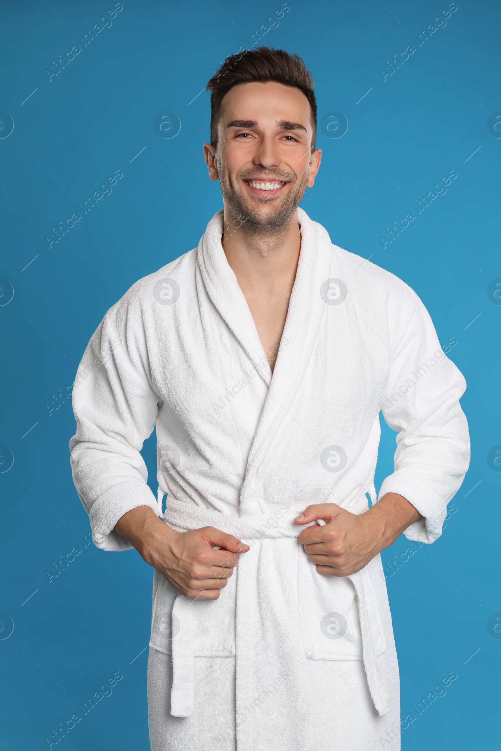 Photo of Happy young man in bathrobe on light blue background