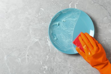 Woman washing dirty plate at grey marble table, top view. Space for text