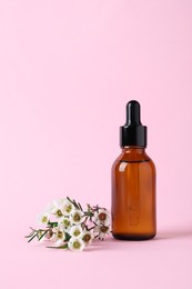 Bottle with cosmetic oil and flowers on pink background, space for text