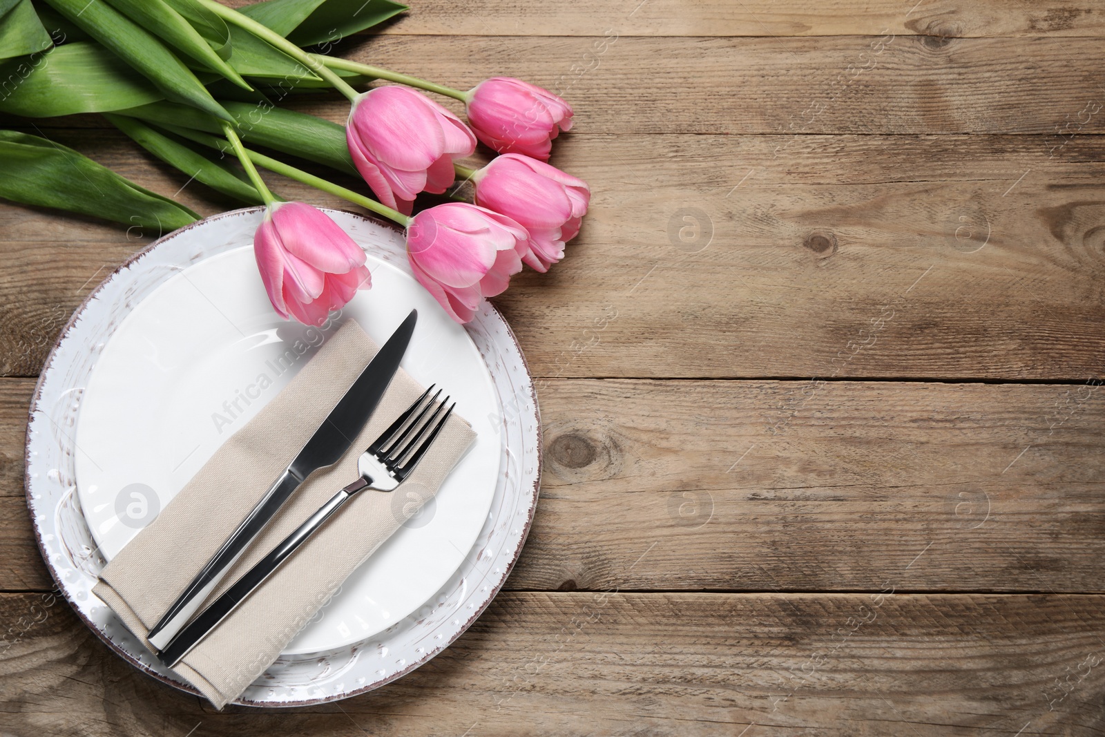 Photo of Stylish table setting with cutlery and tulips on wooden background, flat lay. Space for text