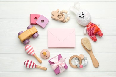 Photo of Baby shower party. Envelope surrounded by gift box and stuff for child on white wooden background, flat lay
