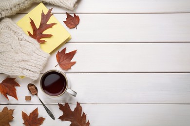 Photo of Cup of hot tea, sweater, book and autumn leaves on white wooden table, flat lay. Space for text