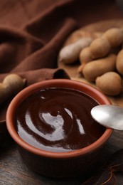 Photo of Bowl of tamarind sauce, spoon and fresh pods on wooden table