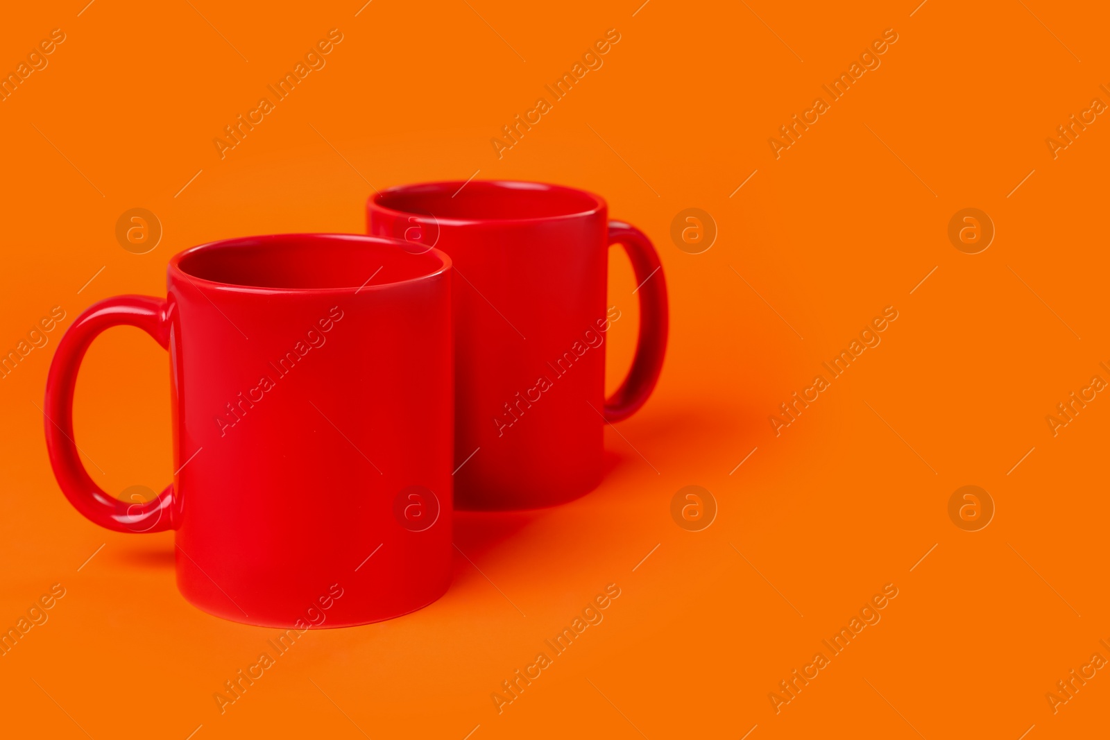 Photo of Two red ceramic mugs on orange background. Space for text