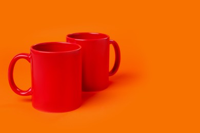 Two red ceramic mugs on orange background. Space for text