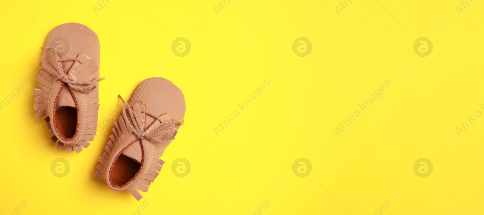 Image of Cute baby shoes on yellow background, top view. Banner design with space for text
