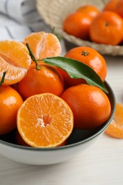 Delicious tangerines with green leaves in bowl on white wooden table, closeup