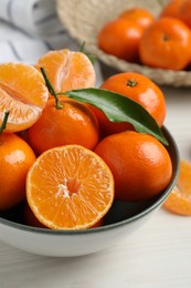 Photo of Delicious tangerines with green leaves in bowl on white wooden table, closeup