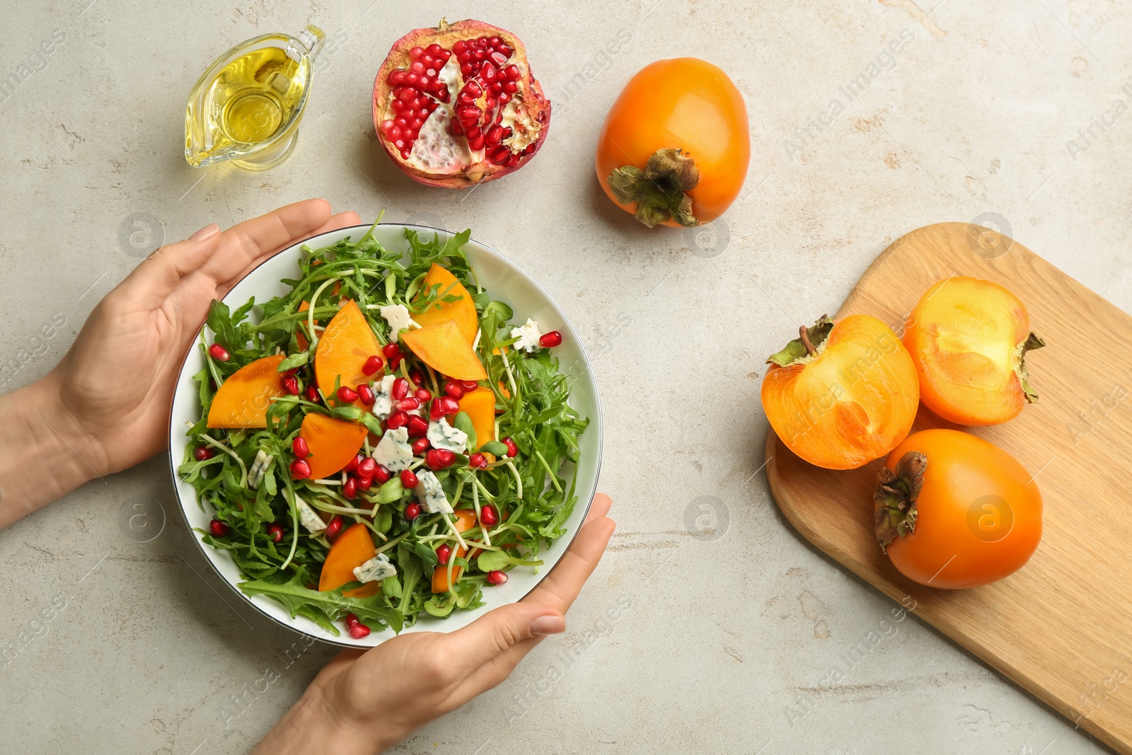 Photo of Woman holding bowl of delicious persimmon salad at light grey table, top view