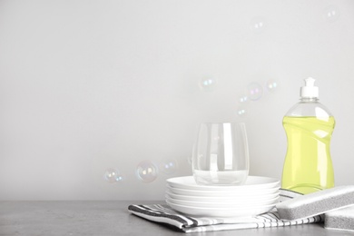 Photo of Cleaning product, plates and soap bubbles on grey background, space for text. Dish washing supplies