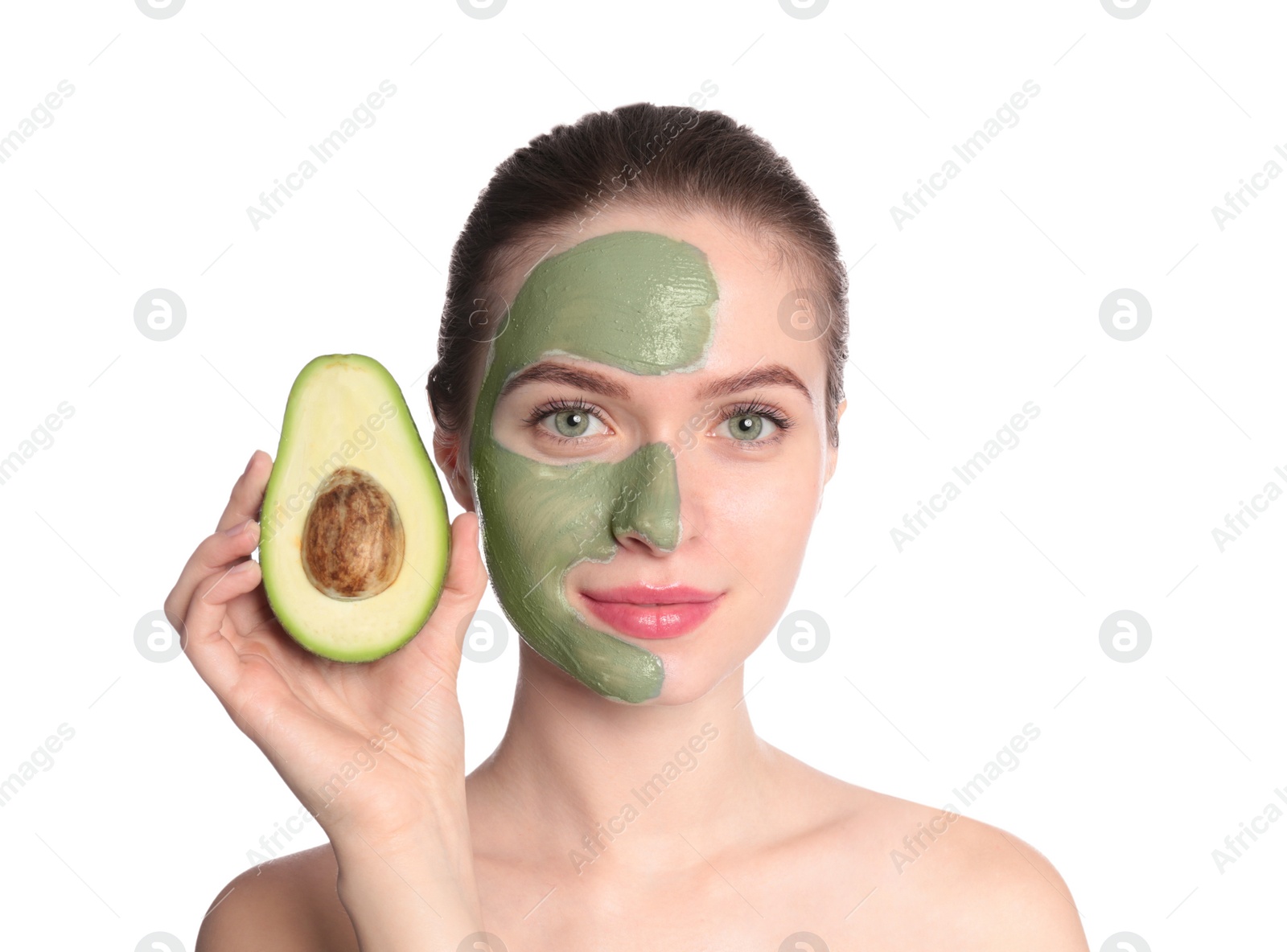 Photo of Young woman with clay mask on her face holding avocado against white background. Skin care